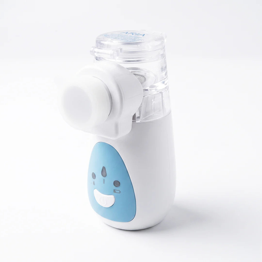 A compact handheld facial cleansing brush with a white body, a light blue front panel featuring a cartoon face, and a clear transparent top cap, shown on a clean white background.